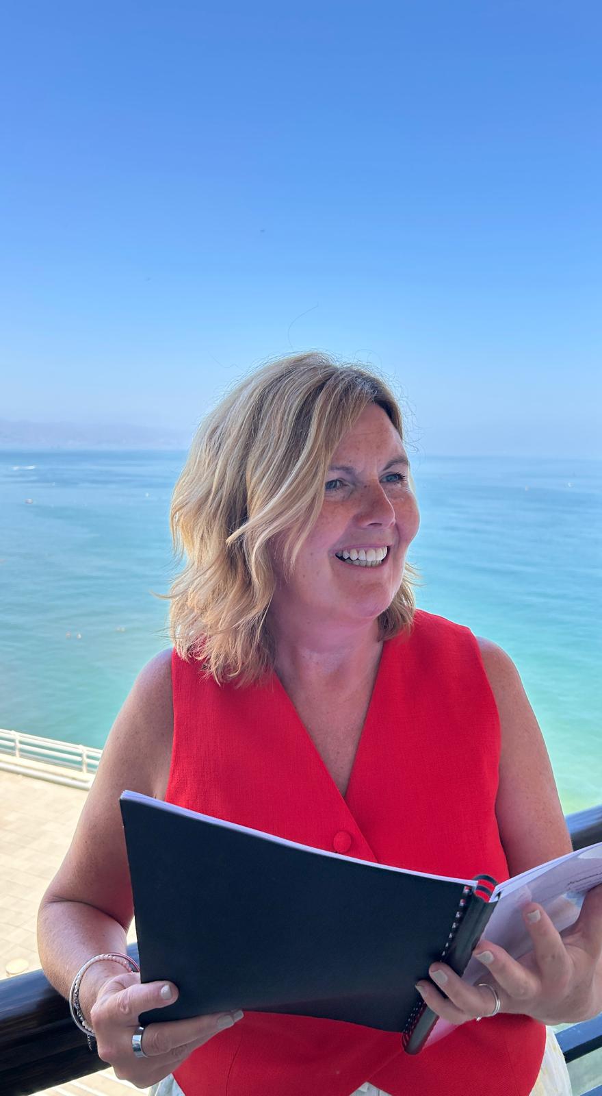 Grá smiling in a red dress while delivering a ceremony by the sea