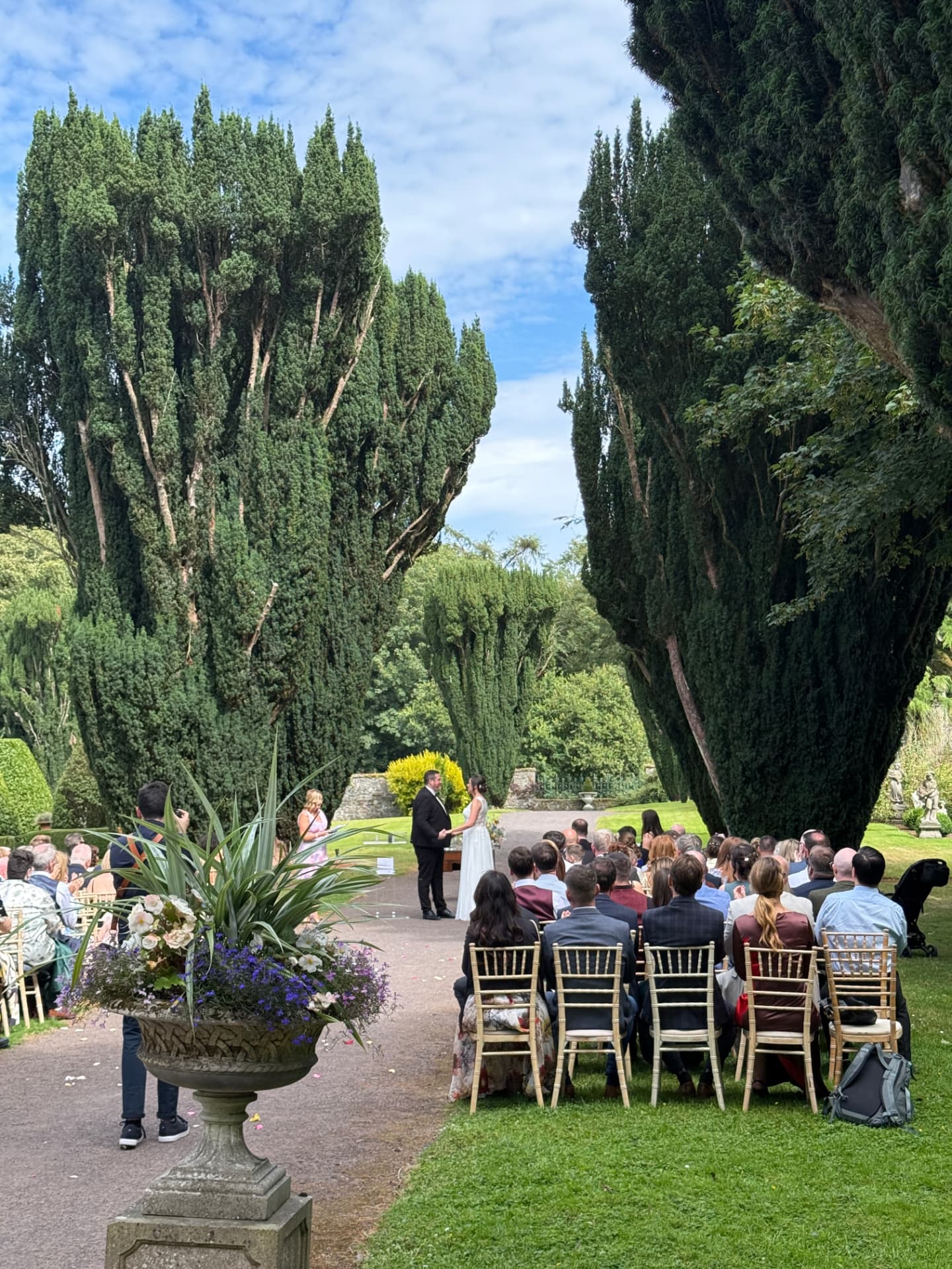 Laure and Dan exchanging vows in a formal garden lined with cypress trees